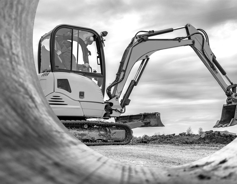 Mini excavator at the construction site on the edge of a pit against a cloudy blue sky. Compact construction equipment for earthworks. An indispensable assistant for earthworks
